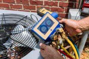 A person uses a digital gauge manifold to check refrigerant levels on an outdoor air conditioning unit next to a brick wall, perfect for a landing page header showcasing HVAC expertise.
