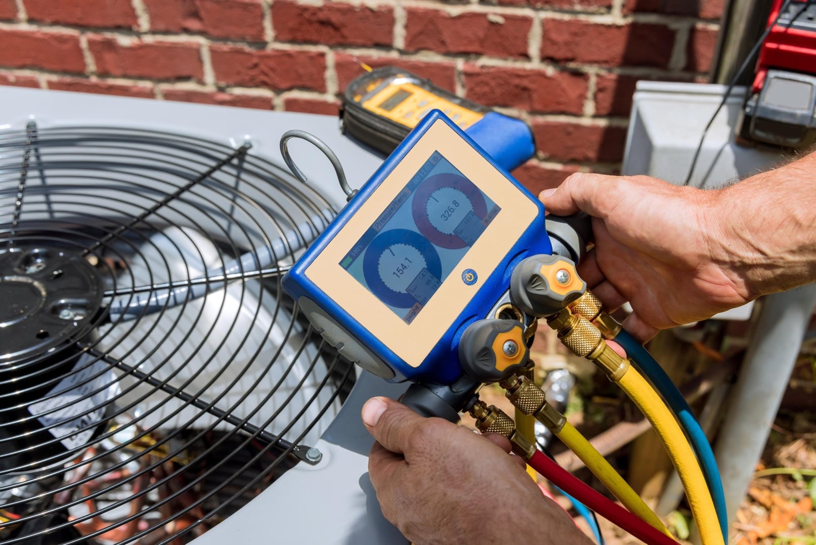 A person uses a digital gauge manifold to check refrigerant levels on an outdoor air conditioning unit next to a brick wall, perfect for a landing page header showcasing HVAC expertise.