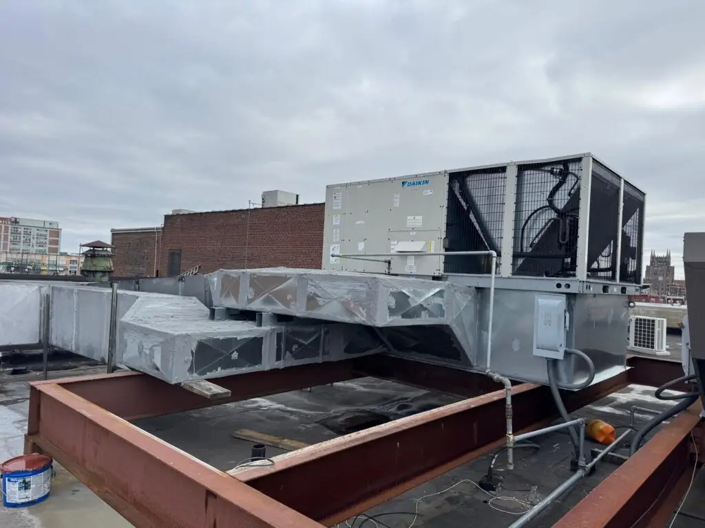 A large commercial HVAC unit installed on a rooftop, ideal for servicing air conditioning or quick commercial air con repairs near me, with ductwork and electrical connections visible under a cloudy sky.