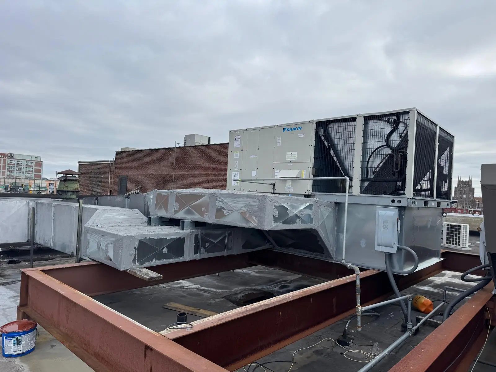 A large commercial HVAC unit installed on a rooftop, ideal for servicing air conditioning or quick commercial air con repairs near me, with ductwork and electrical connections visible under a cloudy sky.