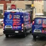Two blue Air Pro HVAC vans, branded with contact details, are parked on a city street near a stop sign—ready to provide fast commercial air con repairs and air conditioner repairing service near me.
