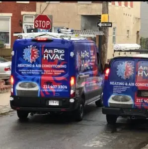 Two blue Air Pro HVAC vans, branded with contact details, are parked on a city street near a stop sign—ready to provide fast commercial air con repairs and air conditioner repairing service near me.