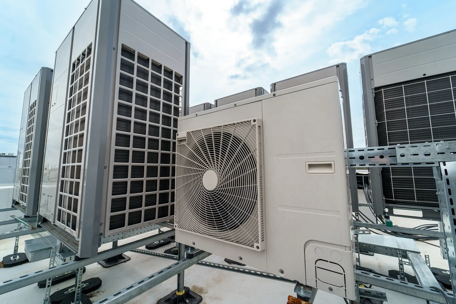 Several large HVAC units are installed on a rooftop, arranged in a row on metal supports with a cloudy sky in the background—ideal for businesses seeking commercial air con repairs or an air conditioner repairing service near me.